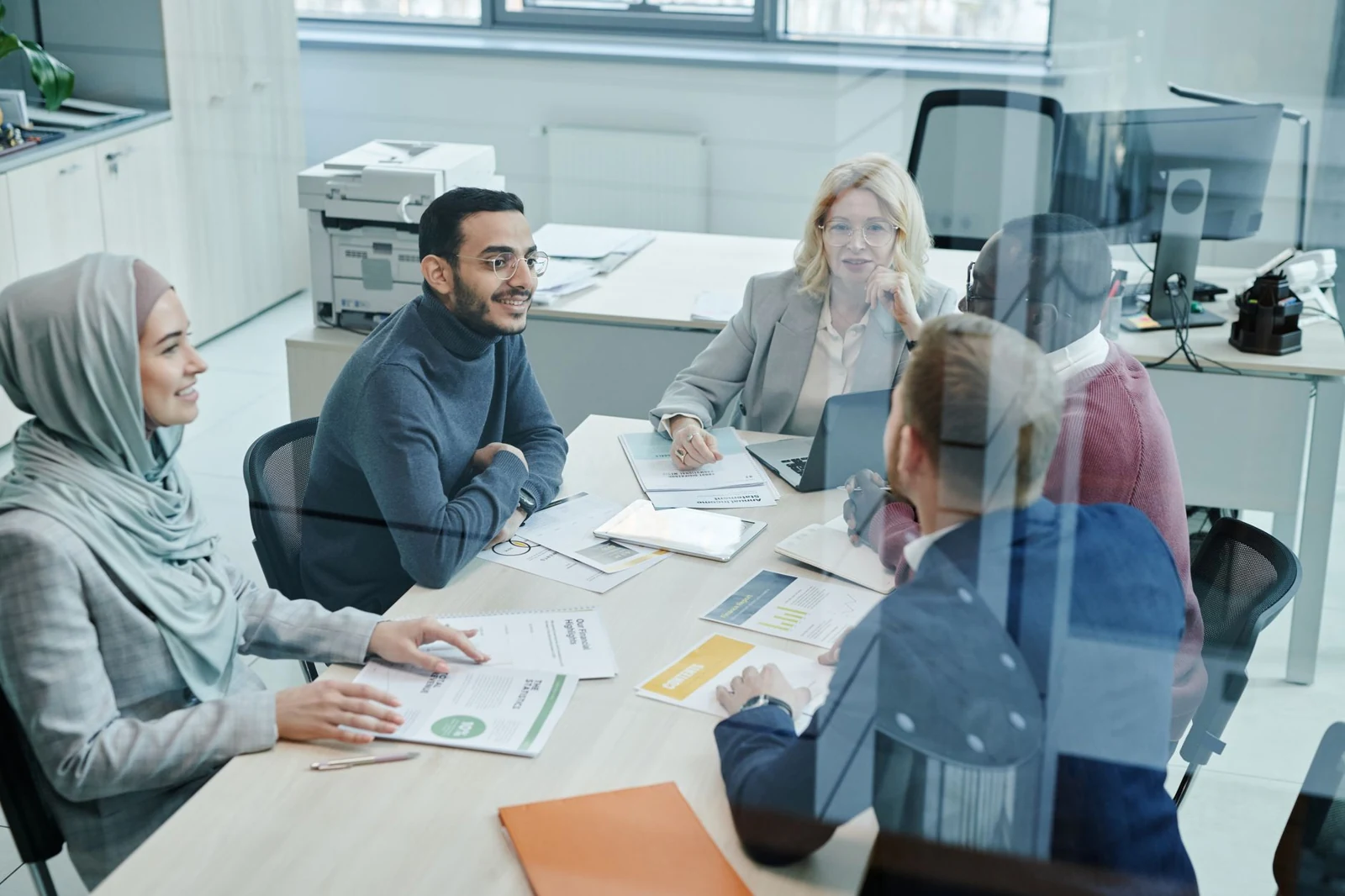 Colleagues discuss documents around a meeting-room table.