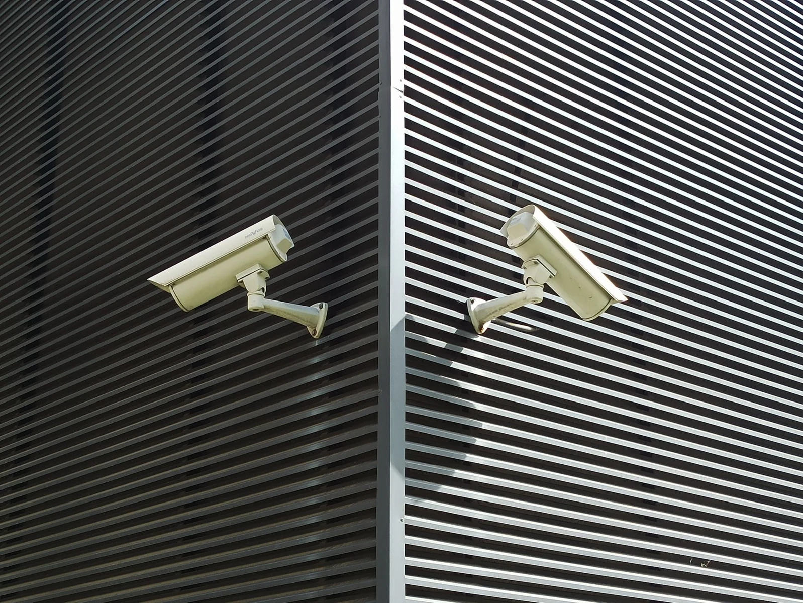 Two surveillance cameras monitor different directions on a building exterior.