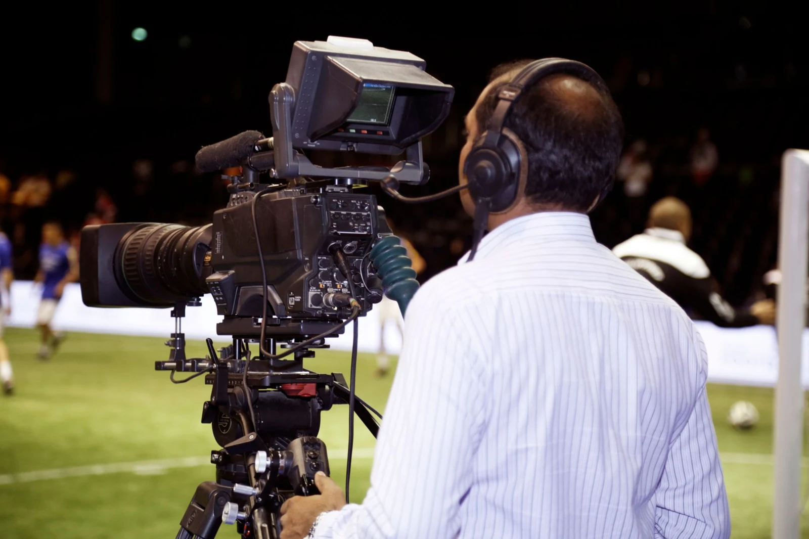 Broadcast camera operator filming a football match from the sideline.